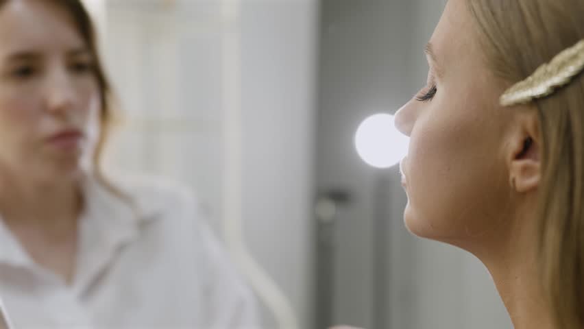 Makeup, beauty salon concept. Female makeup artist spraying spray on model face. Close-up