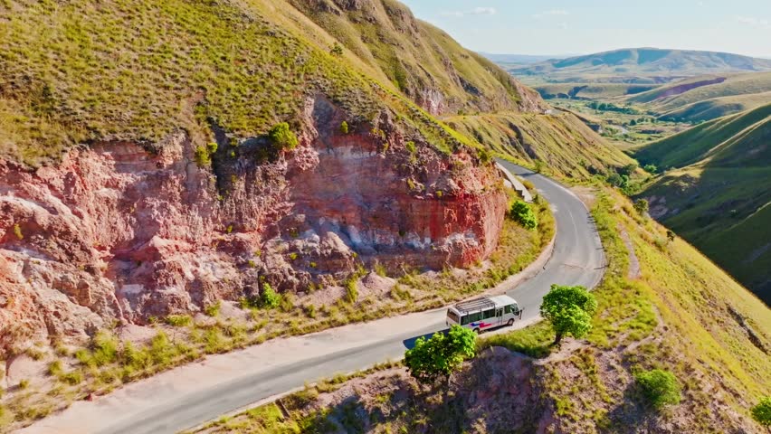 A scenic aerial view of a bus navigating a winding mountain road through the vibrant hills of Madagascar. Remote adventure and striking natural colors captured from above.