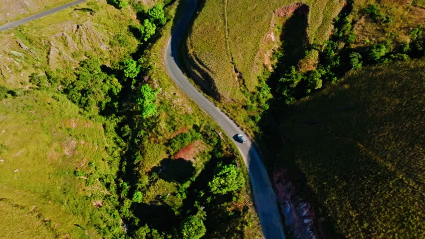 Aerial view of vehicle navigating a winding road through grassy hills and red earth terrain in Madagascar. Ideal for concepts of travel, nature, and adventure.