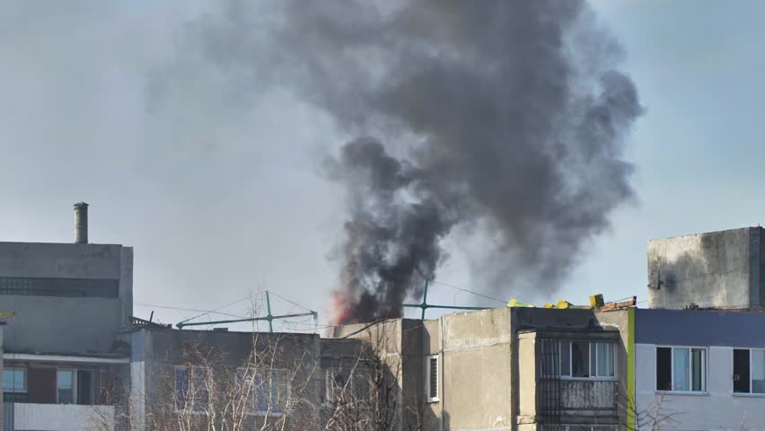 Large column of black smoke rising from burning building roof