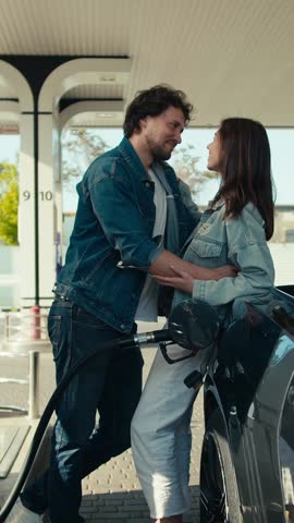 A young couple shares a heartfelt embrace at a gas station under the sun, showcasing love and connection amidst the daily hustle and bustle of city life
