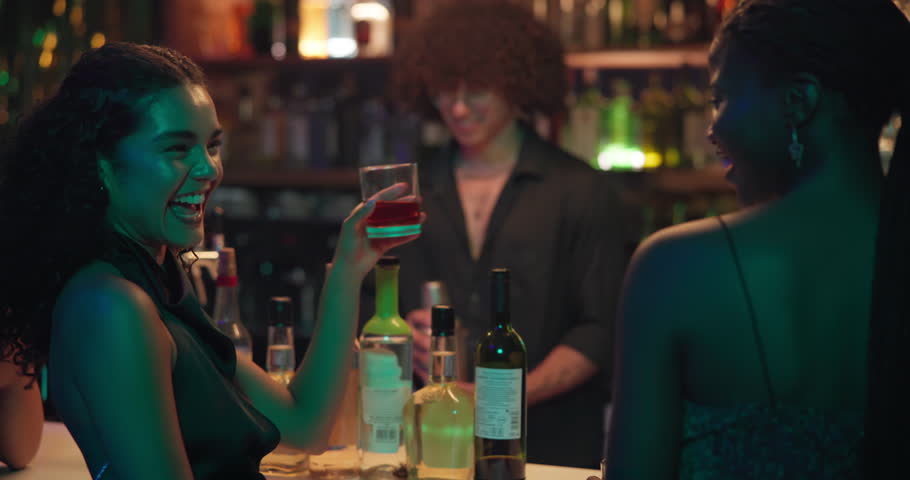 Bartender, women and friends toast at a club for fun, cocktail or happy hour at counter. Man, mixologist and people with alcohol beverage at bar or pub for cheers, social event and party on night out