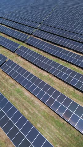 Aerial view of a large solar power plant with rows of photovoltaic panels installed on open land, generating clean renewable energy under a clear sky