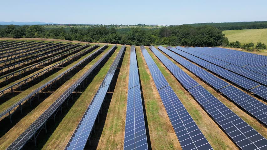 Aerial view of a large solar power plant with rows of photovoltaic panels installed on open land, generating clean renewable energy under a clear sky
