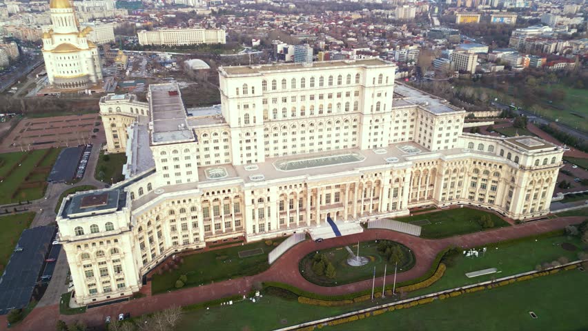 Aerial drone footage of the house of the people in Bucharest. High angle golden hour shot of the  Parliament building in the capital or Romania. Massive governmental structure seen from the air.
