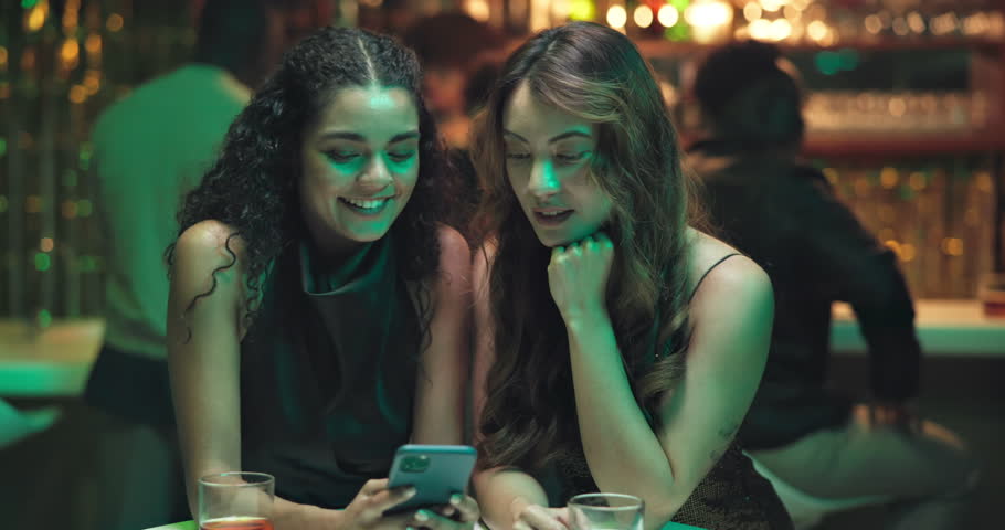 Smile, women and friends with phone at nightclub for browsing, social media and reunion for night out. People, laugh and mobile for funny meme, reading chat and showing memory for bonding together