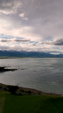 Vertical, aerial: Kaikoura Peninsula landscape, mountain range and oceanfront during the day in New Zealand, pull out drone shot
