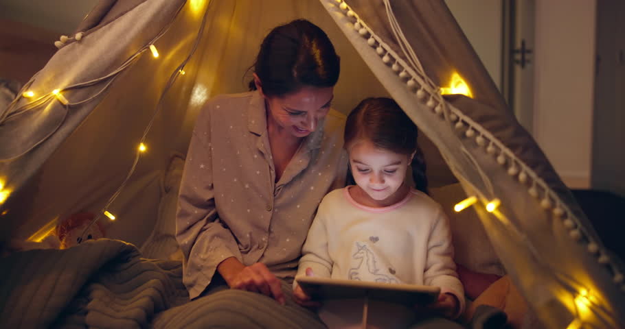 Tent, home and mother with child on tablet for playing game, bedtime story or learning. Online, parent and daughter with tech at night for movie, streaming cartoon and education with happy family