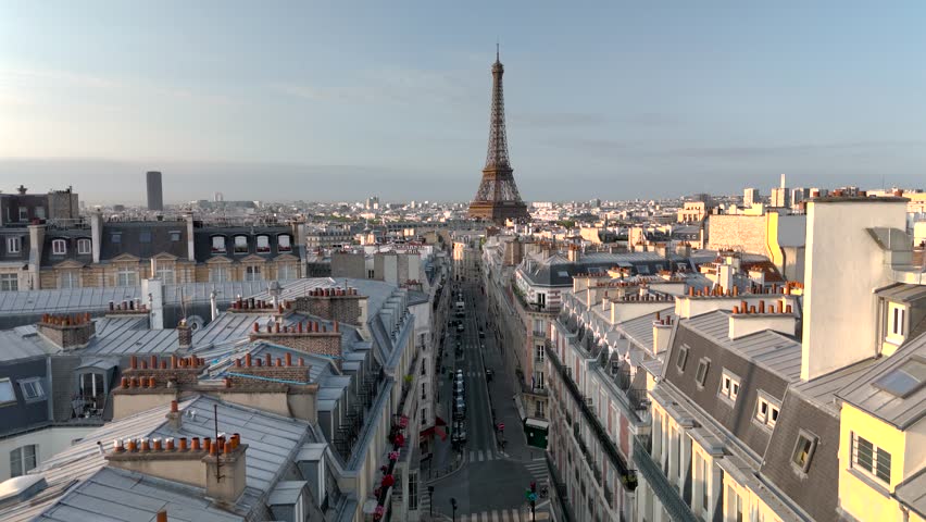 Aerial drone view of the sleepy streets of Paris, France, overlooking the famous Eiffel Tower and Champ de Mars at sunrise or sunset. Low motion over the rooftops. Cinematic 4k. Europe from above.