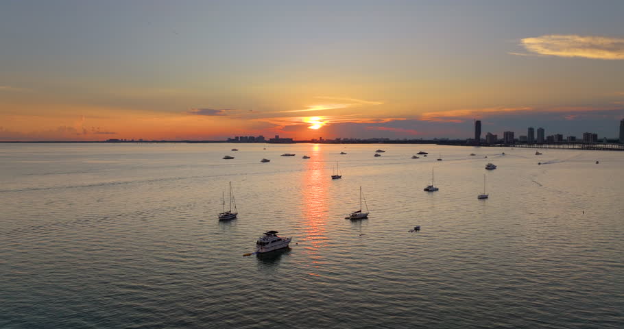 Biscayne Bay harbor in Miami, Florida. Fishing and recreational yachts and boats sailing. Sunset over city skyline with high-rise buildings in downtown.
