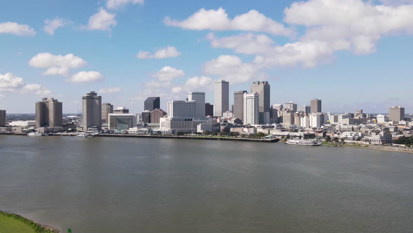 New Orleans, Louisiana skyline seen in a drone timelapse over the Mississippi River on a beautiful day with moving clouds and blue sky