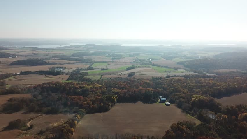 Expansive view of patchy farmland bordered by colorful autumn forest, with Lake Wisconsin gleaming on the distant horizon under bright, clear skies.