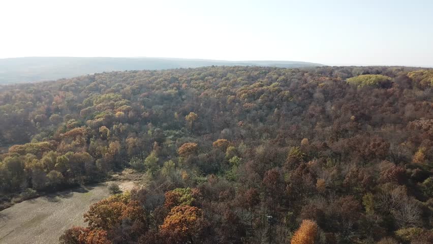 Golden fields and colorful fall foliage spread across the rural landscape with a faint view of Lake Wisconsin on the horizon. A peaceful, expansive Midwestern countryside scene.