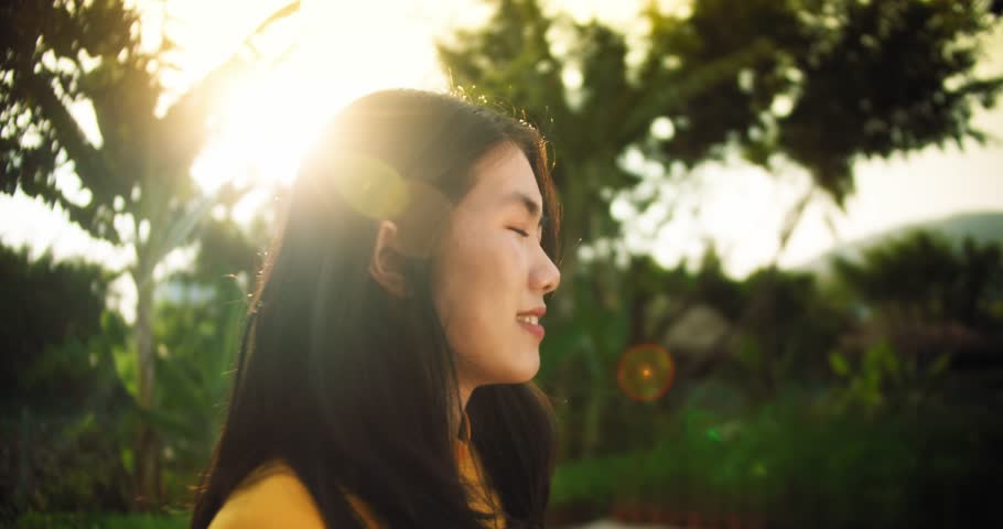 Portrait happy Vietnamese woman looking at the camera, wearing one elegant traditional yellow dress. Beautiful face of a young female girl against a background of tropics who puts on Vietnamese hat.