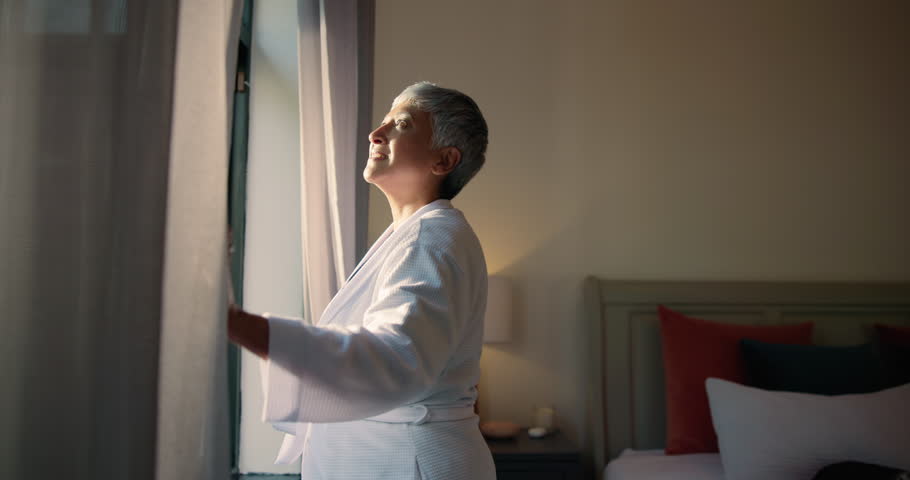 Curtains, morning and smile with old woman in hotel room for accommodation or hospitality. Retirement, wake up and window with happy senior person at lodge or resort for holiday, travel and vacation