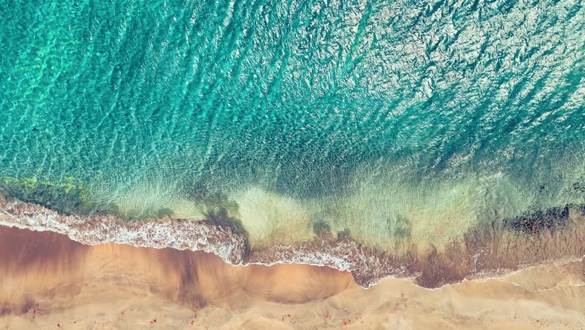 Seamless loop of Atlantic Ocean waves on sandy beach. Top view of waves crashing on tropical beach. Drone view of turquoise blue sea water on golden sand shore.