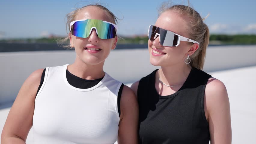 Dynamic Duo Enjoys Playful Moments Together Under the Bright Sun by the Waterfront While Sporting Trendy Athletic Outfits and Stylish Sunglasses