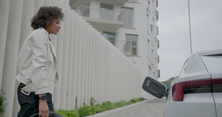 Young Woman Charging Electric Car at Urban Station