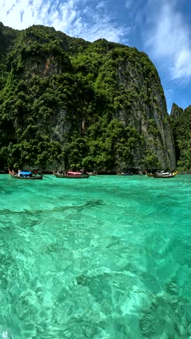 Longtail boats float on turquoise water near rocky islands covered in green trees. The sky is blue with white clouds. Suitable for travel themes, vacation advertisements, or destination marketing.