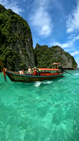 Longtail boats float on turquoise water near rocky islands covered in green trees. The sky is blue with white clouds. Suitable for travel themes, vacation advertisements, or destination marketing.