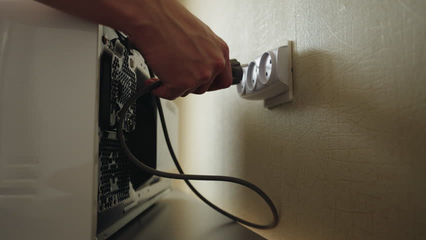 Male hand inserting plug of microwave oven into wall electrical outlet, setting up appliance for use in modern kitchen environment, ensuring proper power connection, close-up, slow motion.
