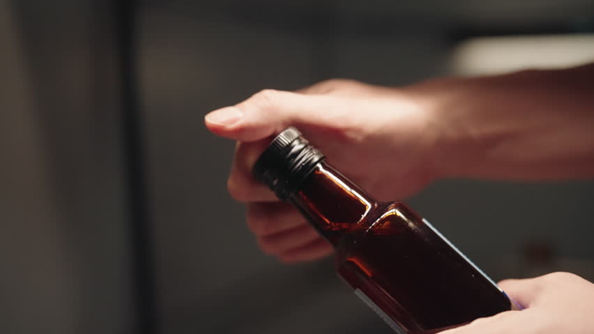 Close-up of male hands opening dark glass bottle of premium cooking oil during preparation for creating culinary in dark kitchen setting. Process of preparing for cooking. Shooting in slow motion.