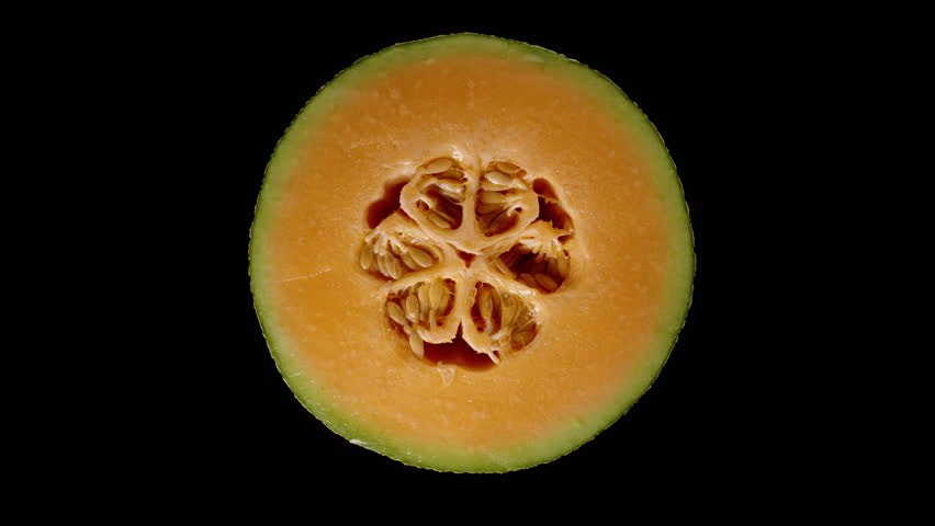 Top View of Cantaloupe Cross Section with Orange Flesh and Clustered Seeds Isolated on Black Background in Seamless Rotation.
