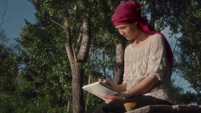 A female artist paints a landscape in watercolor while sitting on a wooden pier near a river