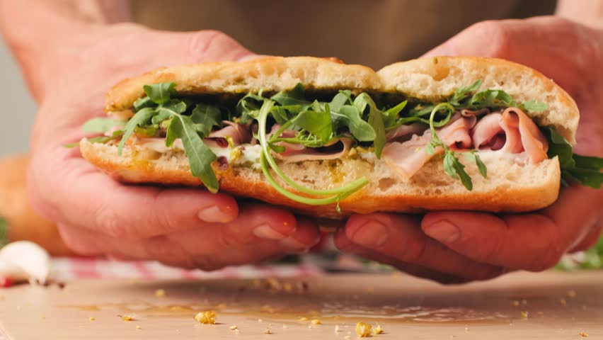 Mortadella ham sandwich, Traditional italian focaccia filled with thin pesto slices of mortadella, served by chef man in cafe restaurant. Macro of traditional italian spanish tapas antipasti. 