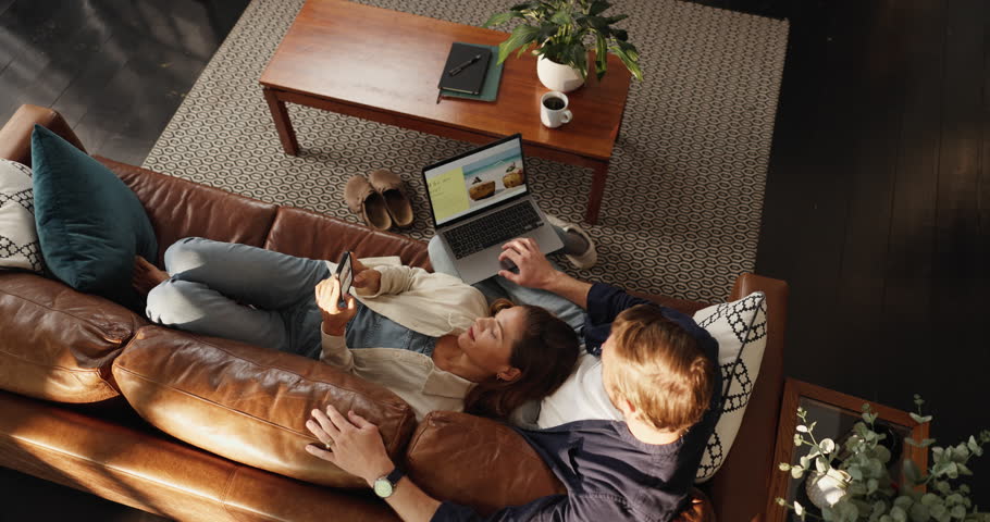 Couple, laptop and sofa with search for holiday location, discount and booking with screen in home. Woman, man and above with computer, smartphone and app for vacation planning in lounge at apartment