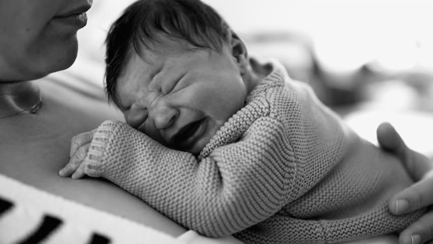 Mother holding a newborn baby close, the infant displays discomfort with furrowed brows, the raw emotions of early parenting and the challenges of soothing a newborn, monochrome