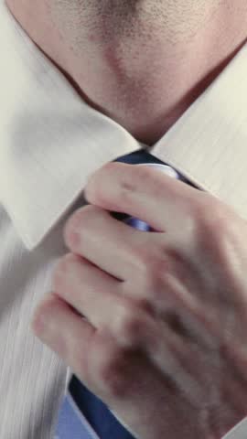 Close-up vertical shot of a man adjusting and tying a necktie, wearing a crisp white dress shirt. A detailed, professional scene ideal for business, fashion, or morning routine concepts.	