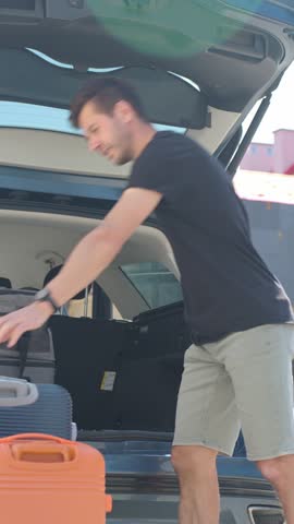 Man loading suitcases into car trunk near suburban house. Preparing for travel by packing luggage into vehicle. Concept of relocation or road trip