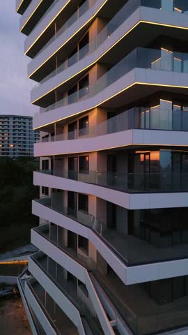 Modern residential building with glass balconies and LED lighting at sunset. Urban architecture and city living concept with soft sky reflections and evening ambiance