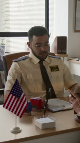 Vertical shot of young bearded male visa officer dressed in uniform stamping customers application rejected and returning it during workday in office