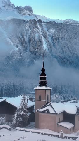 vertical drone shot of Chamonix village in French Alps, alpine village with church bell tower covered with snow, snowy winter landscape in Europe. High quality FullHD footage