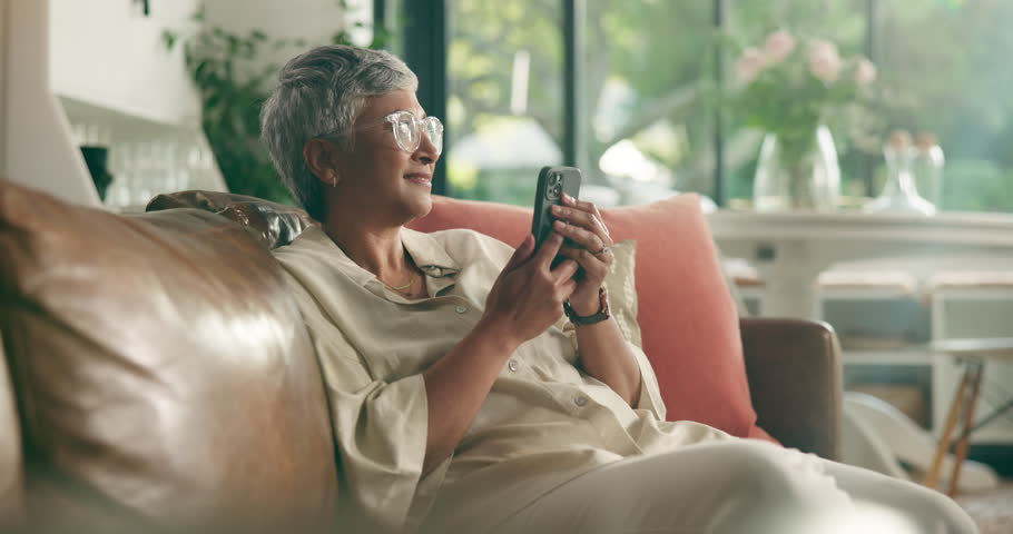 Mobile, think and senior woman in home for emotional message, love and good news for online dating. Phone, smile and person in living room in retirement for reflection, nostalgia or romantic memory
