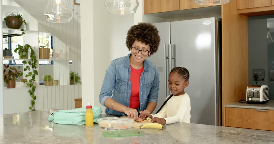 Mother daughter slicing food in kitchen packing lunch boxes, zipping mint-green backpack for school. Family, nourishment, education, nurturing, domestic, harmony, caregiving