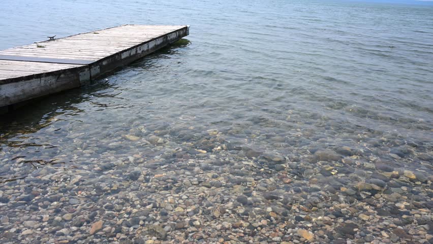 View of an old wooden dock and a stoney beach as small waves ripple of the water surface