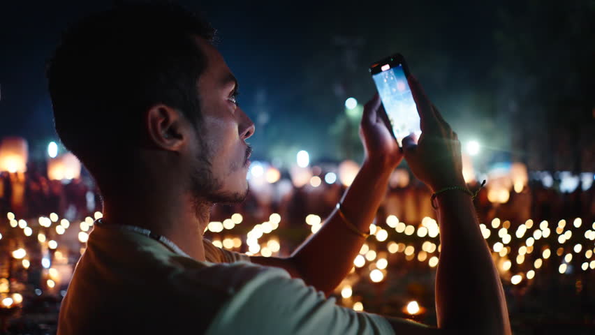 young latin man records a video with his smartphone on the night of the fireworks next to the candles