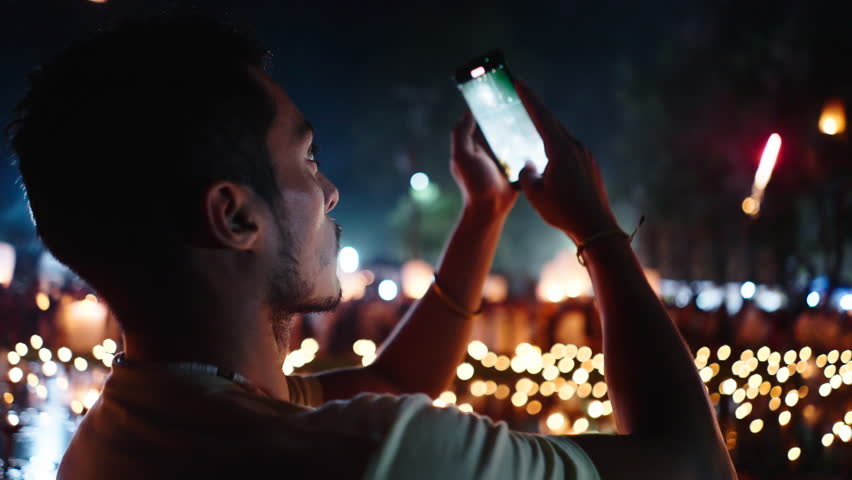 young latin man records a video with his smartphone on the night of the fireworks next to the candles