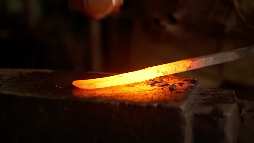 Blacksmith hits red-hot metal on an anvil with heavy hammer. Making blacksmithing items in workshop