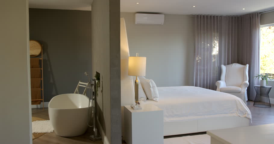 Camera pausing on bathtub faucet, panning right to reveal king bed, armchair, plant in master suite. Luxury, modern, minimalist, tranquility, comfort, naturallight, decor