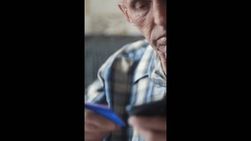 Serious elderly man holding smartphone and bank card making online purchase or communicating with phone scammers, vertical video, concept of senior fraud through internet - Powered by Shutterstock - Get 15% off with code: PIKWIZARD15