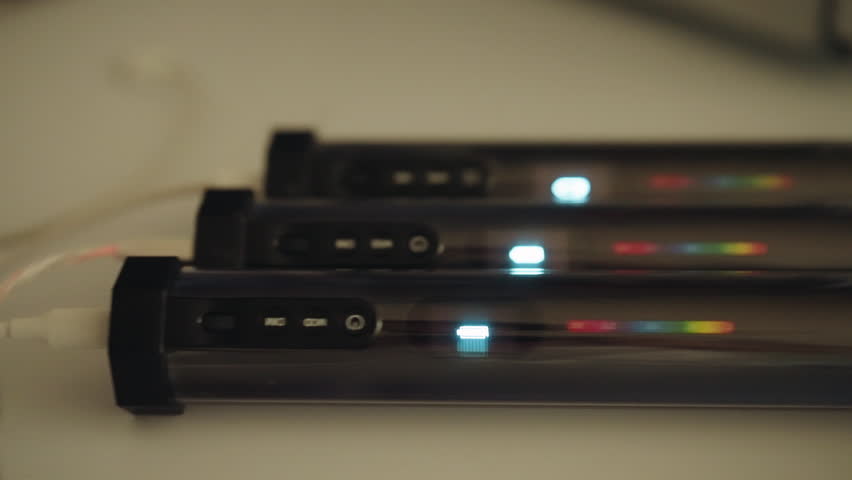 Portable light sticks charging via USB cable, showing diverse battery level. Process preparing photographer and videographer for work with technological accessory for creative visual content, close-up
