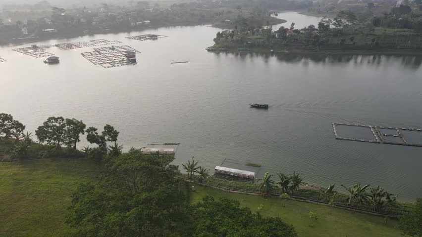 Morning scene of a fisherman on a boat in Padalarang lake, with floating homes and fish farming areas in the background