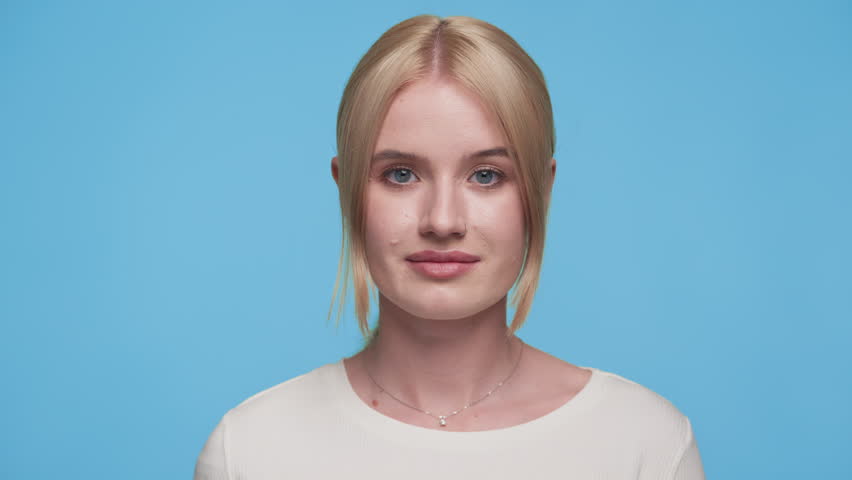 Woman covering eyes with hand playfully on blue background