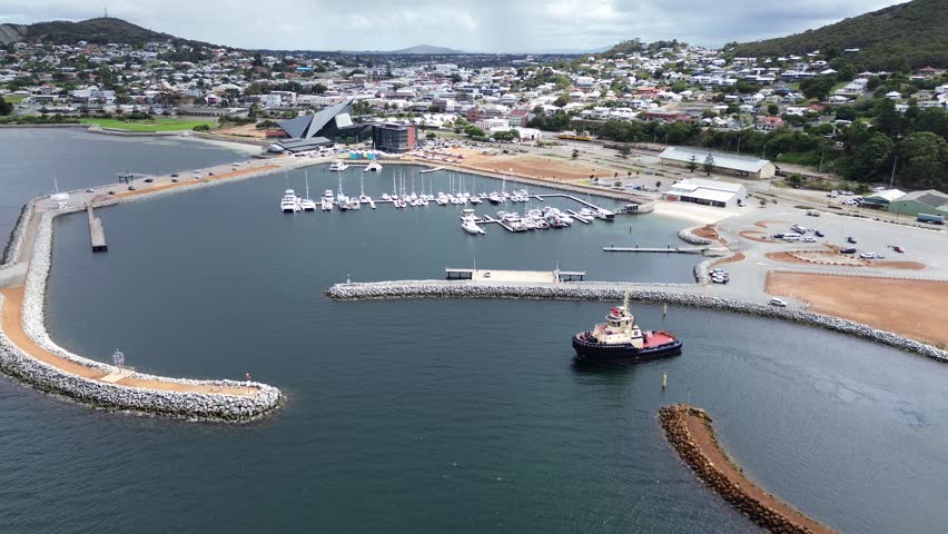 Tug boat leaving a harbour looking down with the town of Albany western Australia nestled between two mountains. Blue still water with a boat Harbour and buildings. Moving footage 