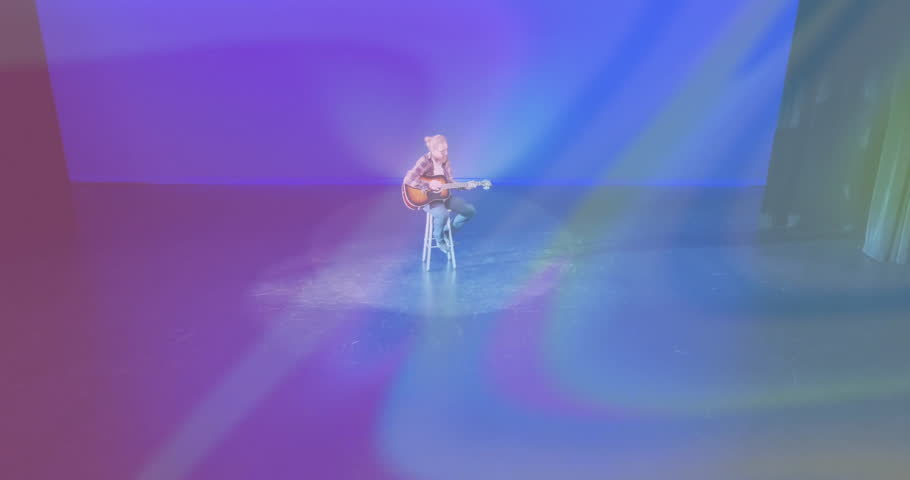 Spotlight activating musician strumming acoustic guitar as rainbow lights shifting for music promo. Music, performance, stage, lighting, atmosphere, artistry, concert
