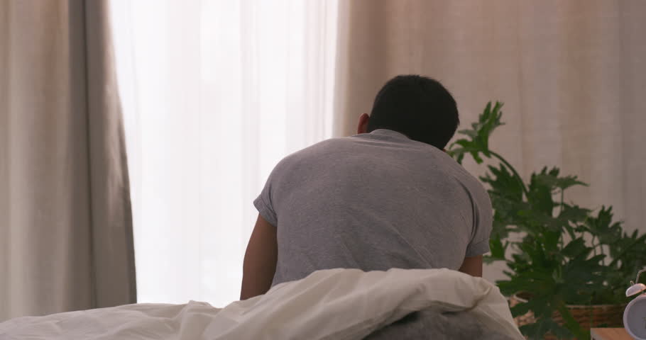 Tired, wake up and back of man in bedroom with insomnia, fatigue and exhausted in house. Apartment, sleepy and moody person in bed for lazy, frustrated and upset in morning with no sleep in home